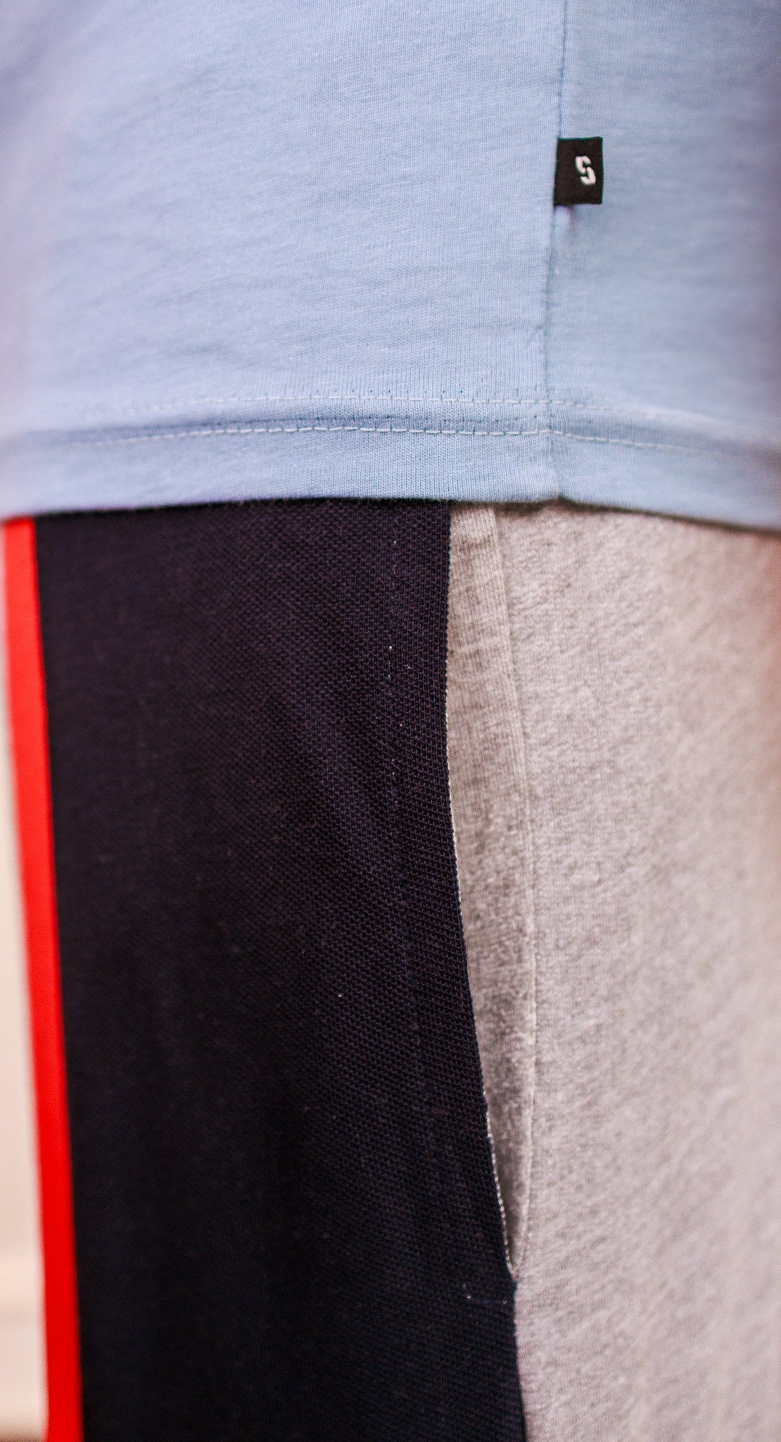 Close-up of a light blue shirt with a brand logo, black pants with red stripe, and gray pants.