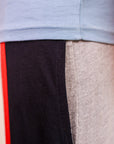 Close-up of a light blue shirt with a brand logo, black pants with red stripe, and gray pants.