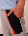 Person wearing gray sweatpants with a black and red stripe, light blue shirt, blurred background