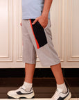Person wearing gray shorts with a red stripe, light blue shirt, and white sneakers in a kitchen.