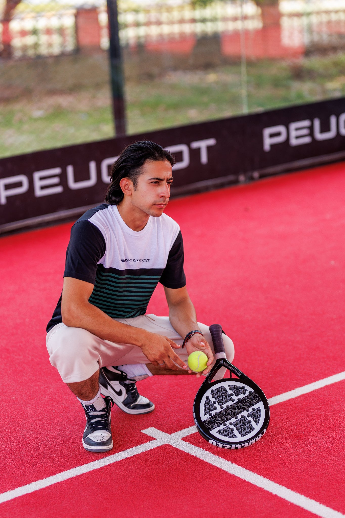 Person on a tennis court holding a racket and ball, with a Peugeot advertisement in the background.
