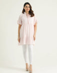 A mid-length pastel pink top with ruffle details and half sleeves, paired with white pants. The top features a V-neck with a frill and drawstring opening, and is displayed on a female model.