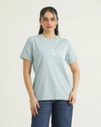 A woman wearing a pastel blue printed t-shirt with round neck, binding, contrast print, and turn-up half sleeves, paired with blue jeans.
