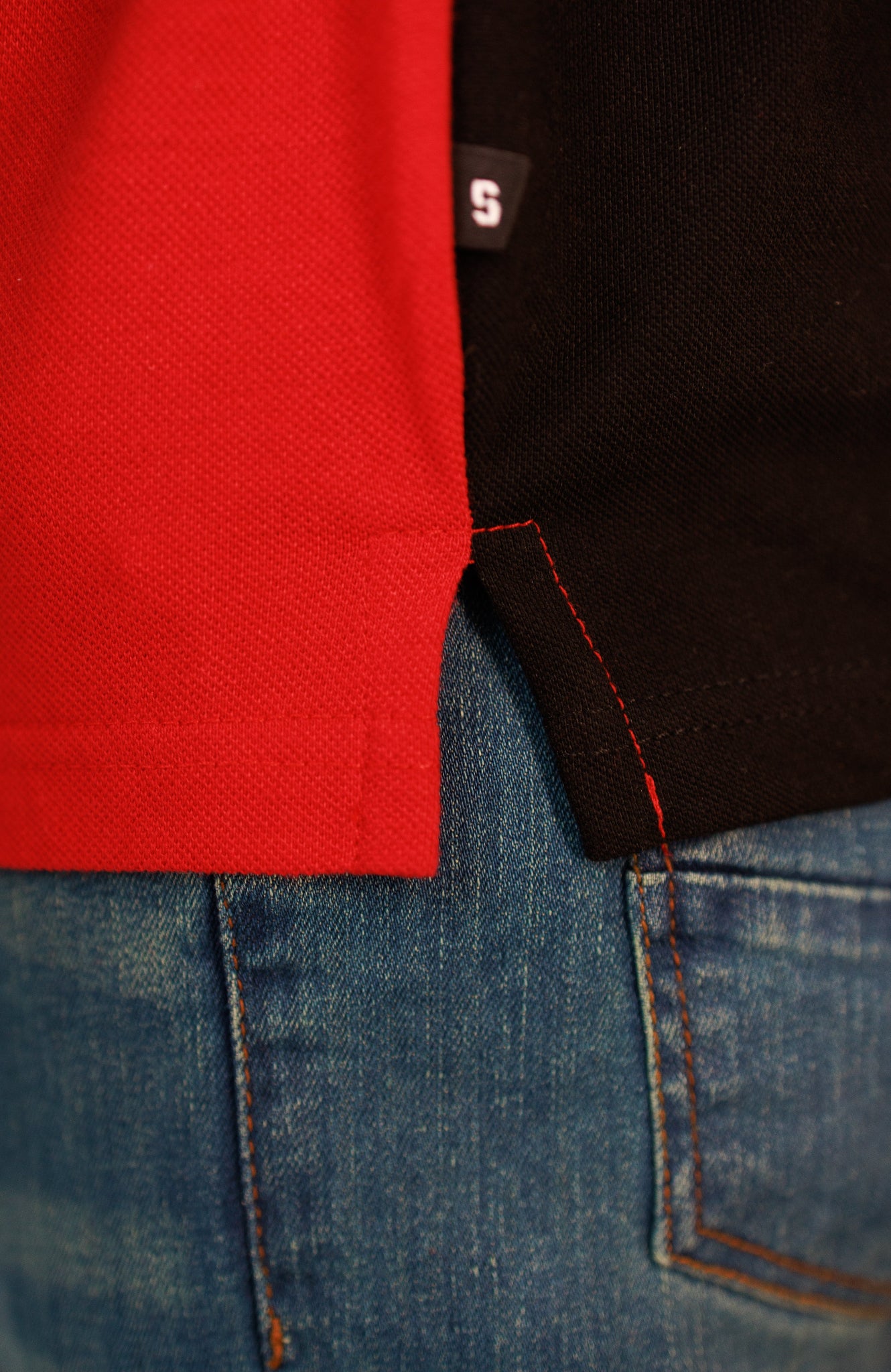 Close-up of a red shirt, black jacket, and blue jeans with a brand logo.
