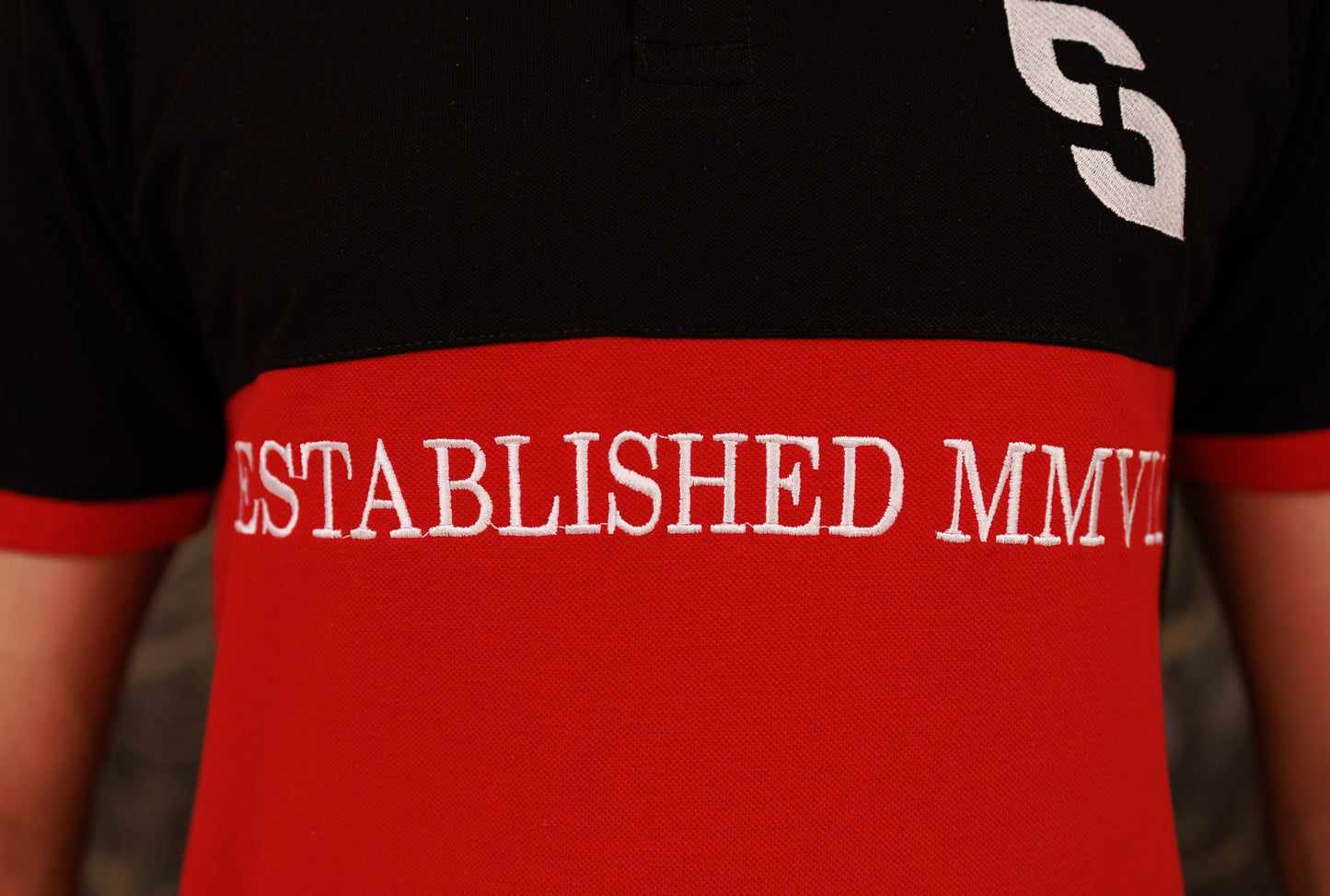 Black t-shirt with red band displaying 'ESTABLISHED MMV' on a blurred background