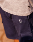 Navy pants with a logo on the pocket worn by a person, blurred background