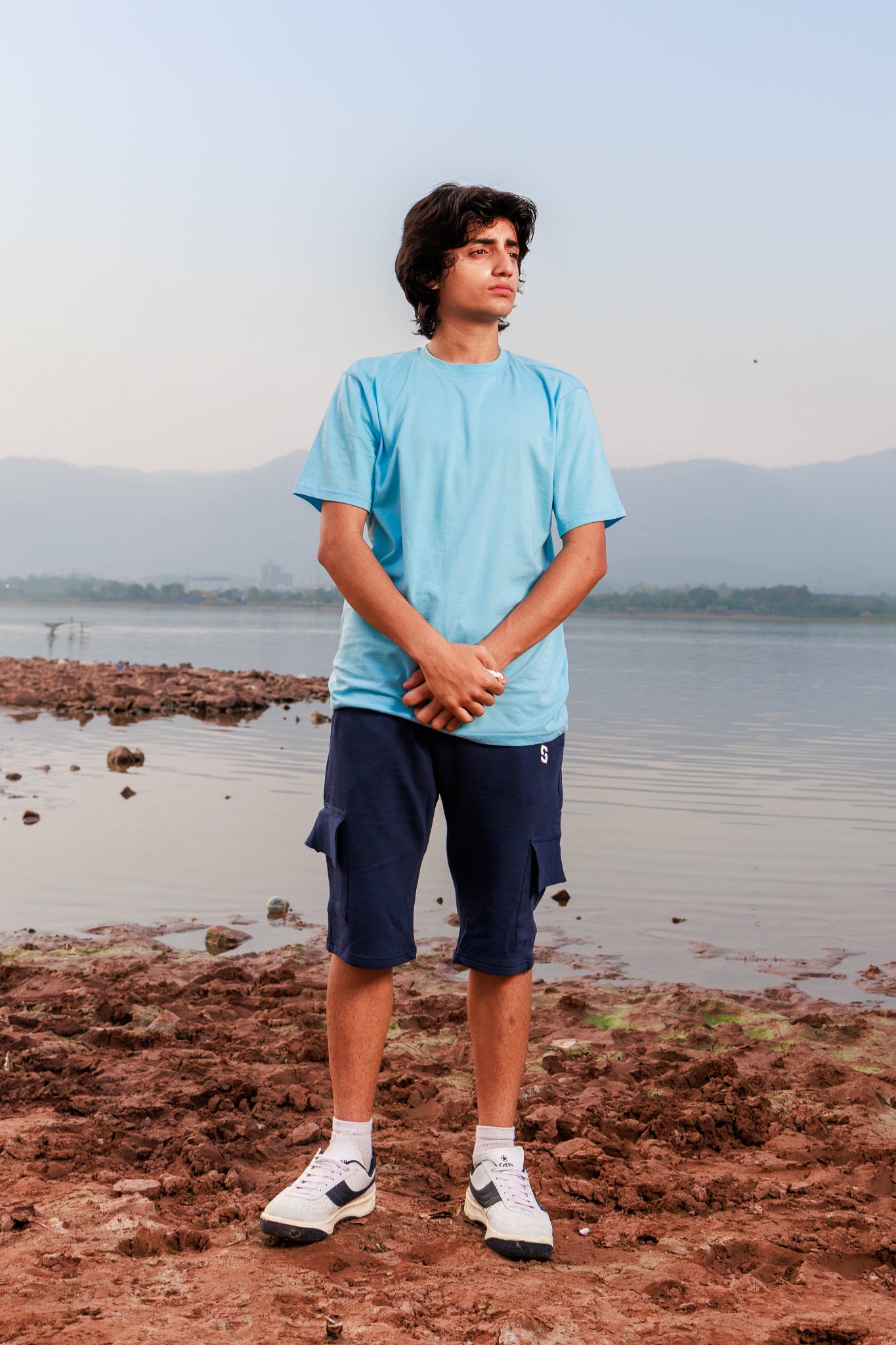 Person standing on a rocky shore with water and mountains in the background