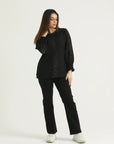 A woman standing against a white background wearing black straight leg denim jeans and a black top with long sleeves.