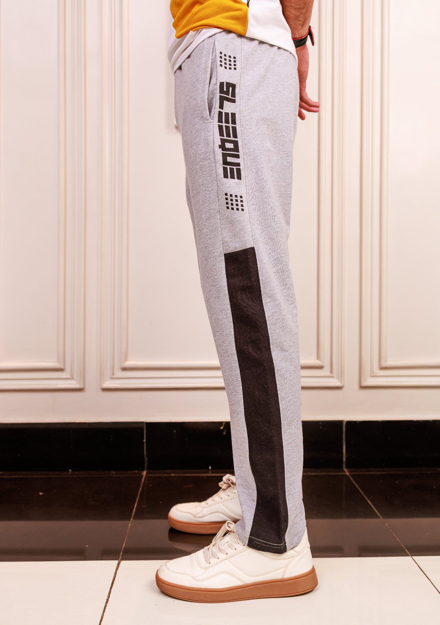 Person wearing gray jogger pants with black accents and white sneakers in a room.