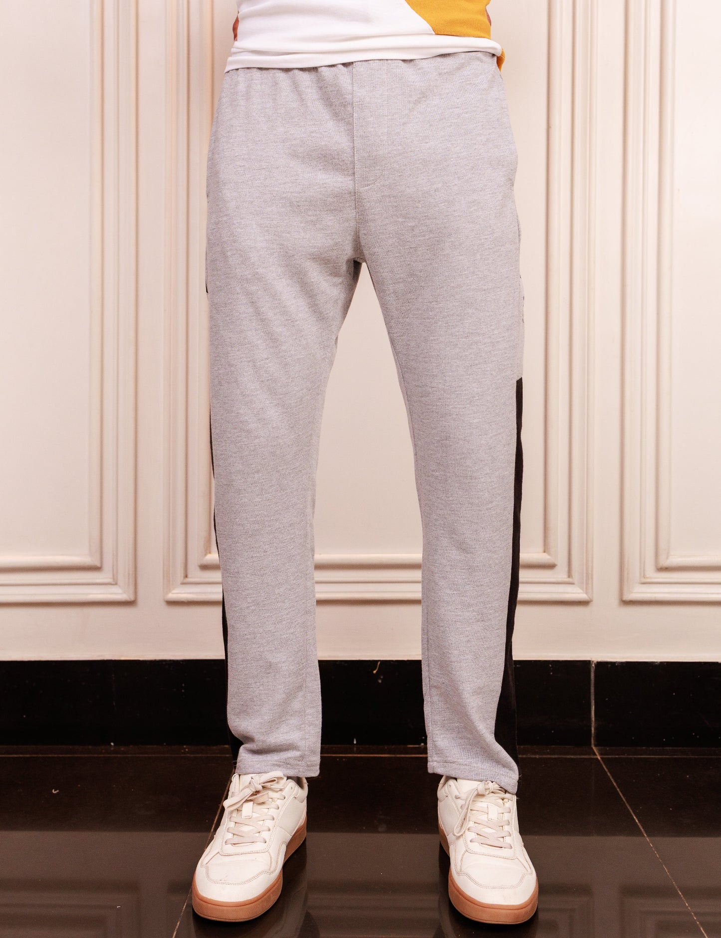 Person wearing gray sweatpants and white sneakers in a room with beige walls.