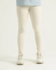 A pair of beige leggings on a female model, paired with a blue top and white sneakers.