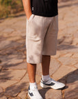 Person wearing beige shorts and white sneakers on a stone pavement