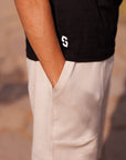 Person wearing a black shirt with a white logo and beige pants against a blurred background