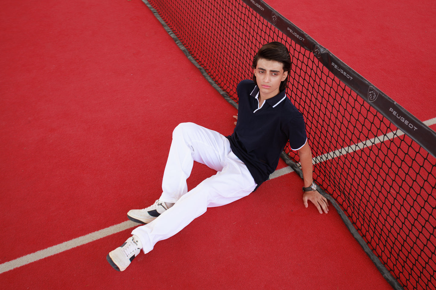 Person sitting on a red tennis court next to the net