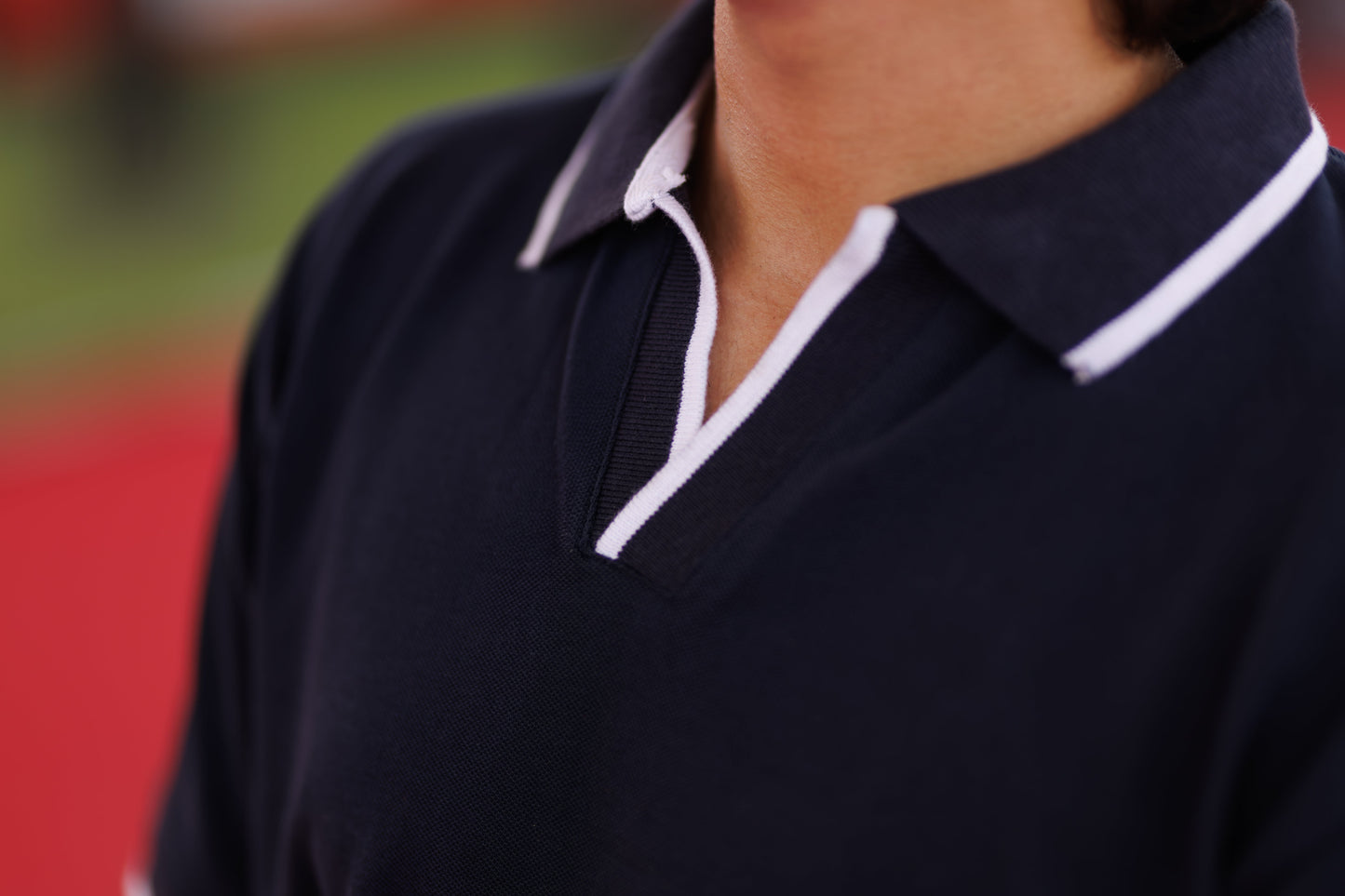 Navy polo shirt with white trim worn by a person on a blurred background