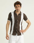 A man wearing a short-sleeved, button-placket, piqué collar shirt with white and brown panels and a straight-cut hem with slits at each side.