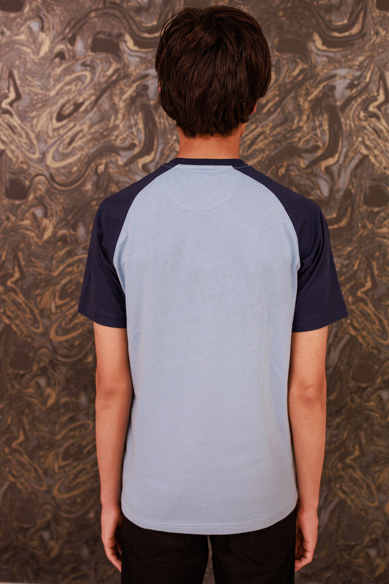 Person wearing a gray and navy baseball shirt against a textured brown background