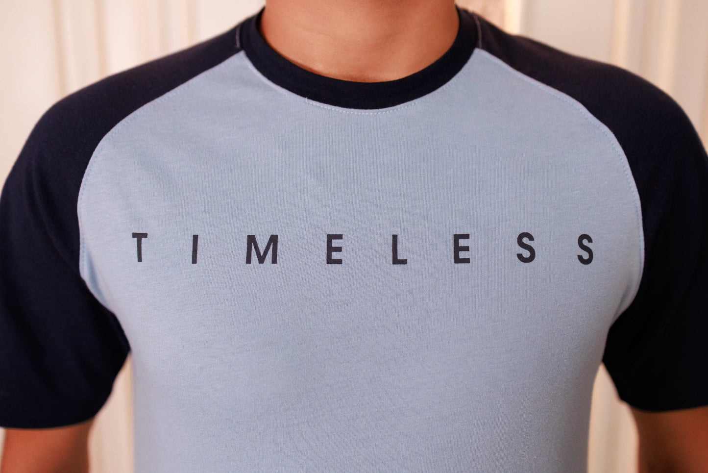 Gray and black baseball shirt with 'TIMELESS' text on a neutral background