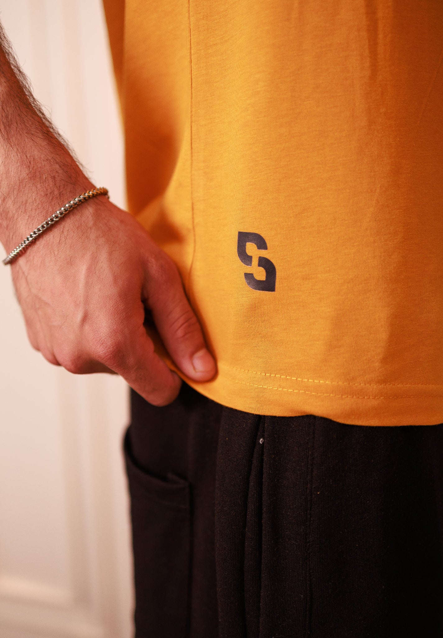 Person wearing a mustard yellow t-shirt with a logo, standing against a neutral background.