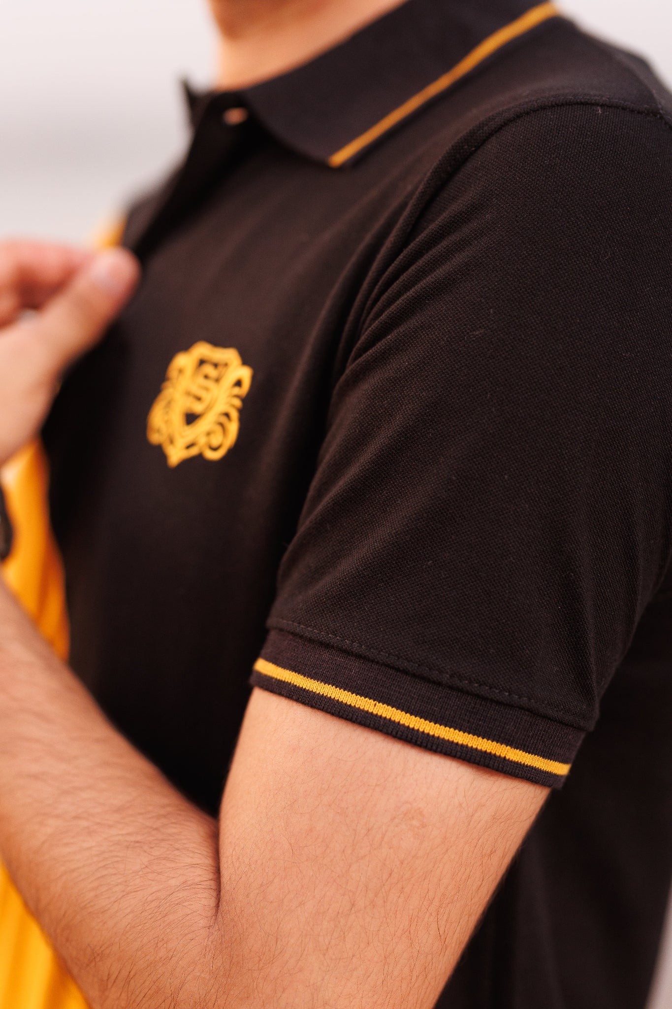 Black polo shirt with yellow trim and logo on a neutral background