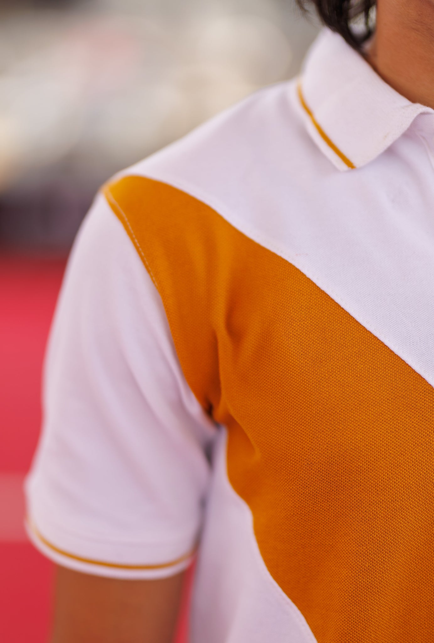 Close-up of a person wearing a white and orange polo shirt with blurred background