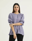 A woman wearing a long-sleeved, hip-length top in a muted lavender hue with all-over raised dot motifs, featuring a round neckline with a back slit opening, 3/4 length puff sleeves with elasticated smocking at the hem, and a straight cut.