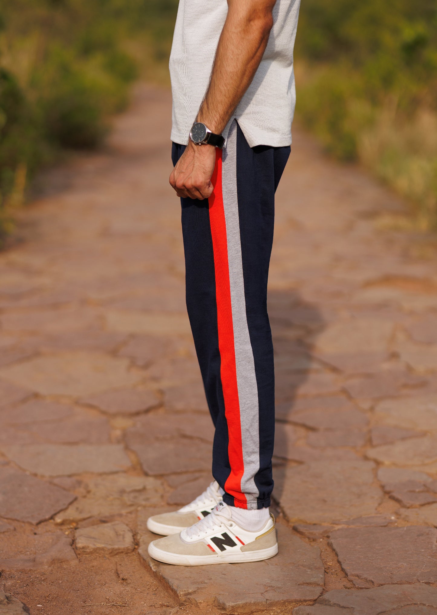 Person wearing navy track pants with red and gray stripes on a stone path.