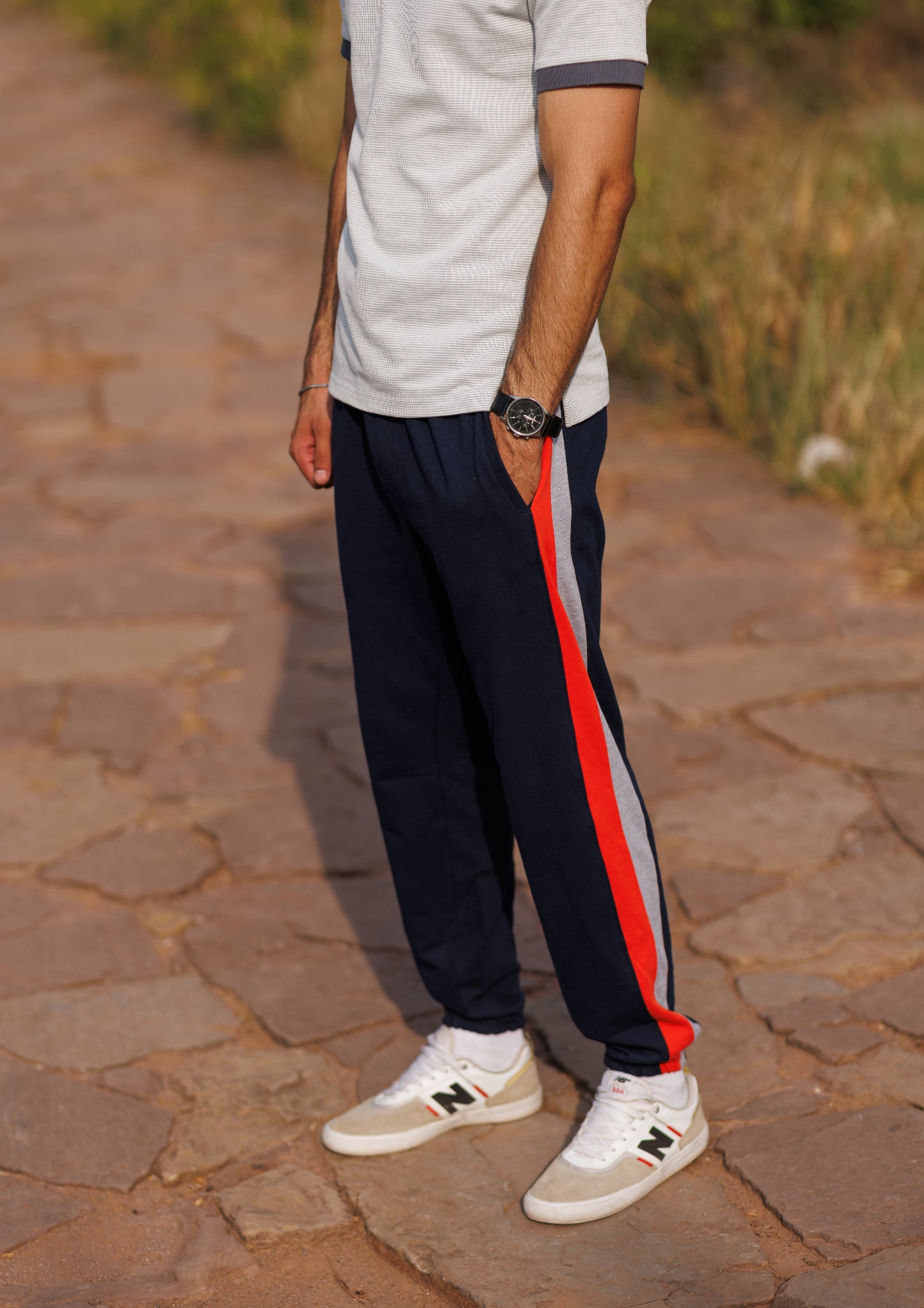Person wearing black pants with red and white stripes, a light gray shirt, and white sneakers on a stone path.