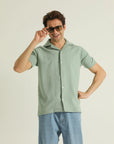 A man wearing a green, short-sleeved, button-up shirt with a collar, displaying a textured knitted design.