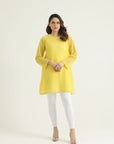 A woman wearing a mustard yellow chikenkari top with long straight sleeves and a round neck. The top has a back opening and under lining attached.