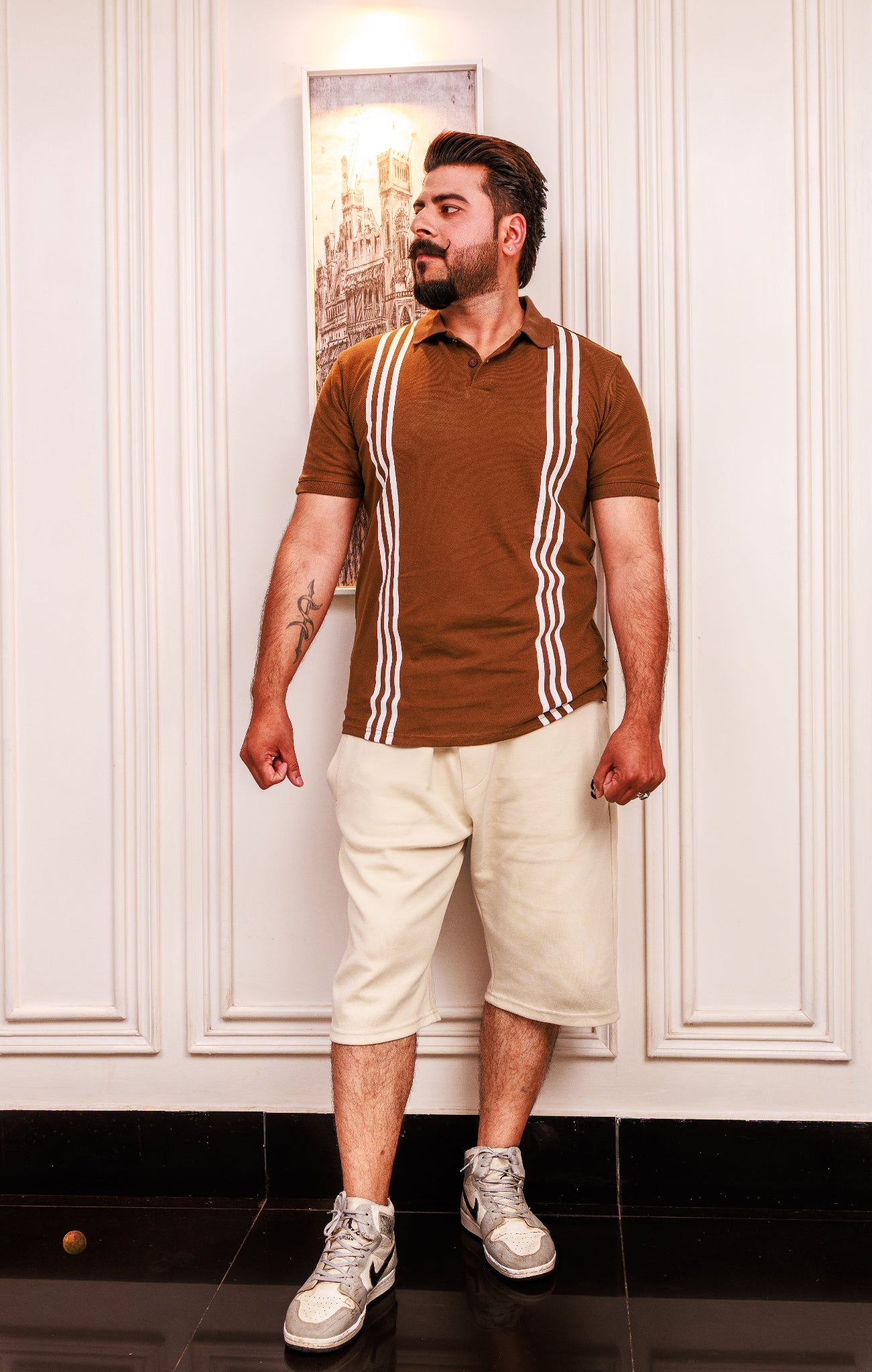 Man wearing a brown polo shirt with white stripes and beige shorts indoors.
