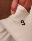 Close-up of beige pants with a logo on the pocket, worn by a person in a brown sweater.