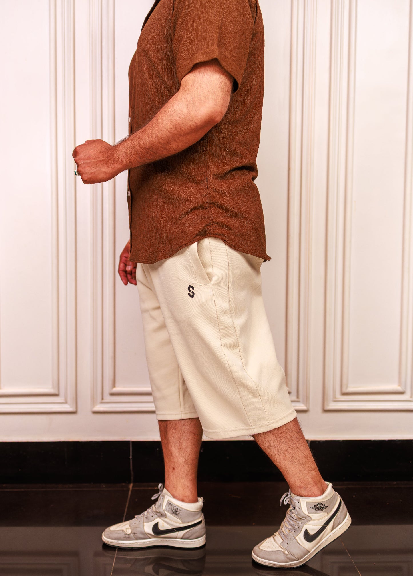 Person wearing a brown shirt, beige shorts, and gray Nike sneakers in a kitchen.