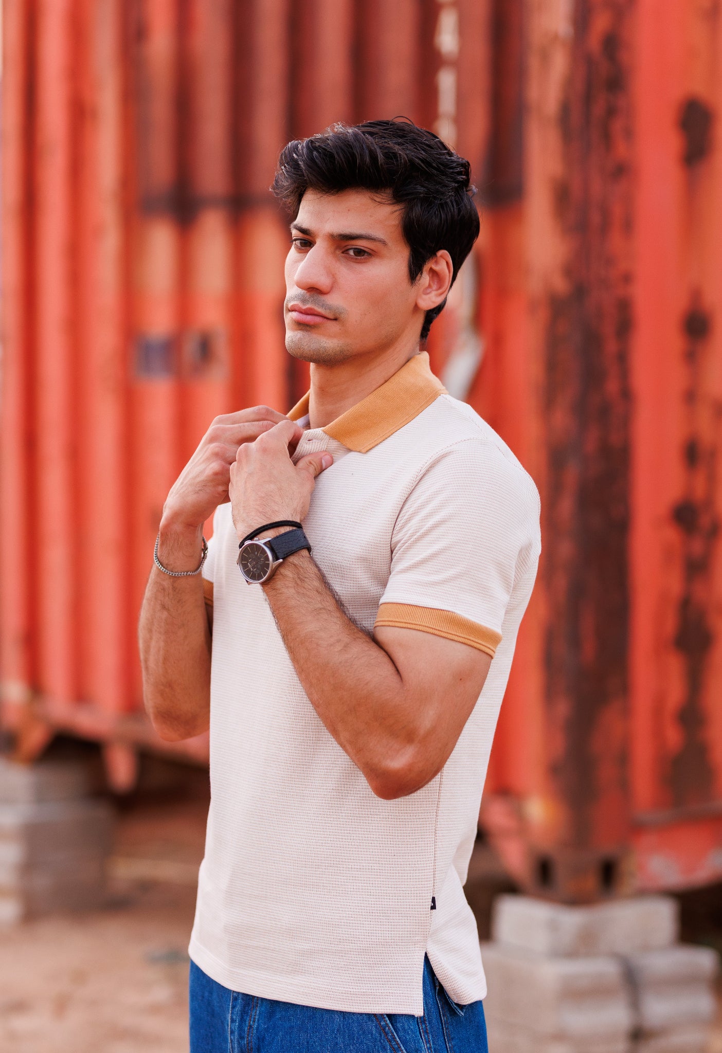 Man adjusting his collar in front of orange shipping containers