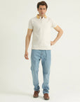 A man standing against a white background wearing a white short-sleeved polo shirt with a collar and button placket, and light blue jeans.