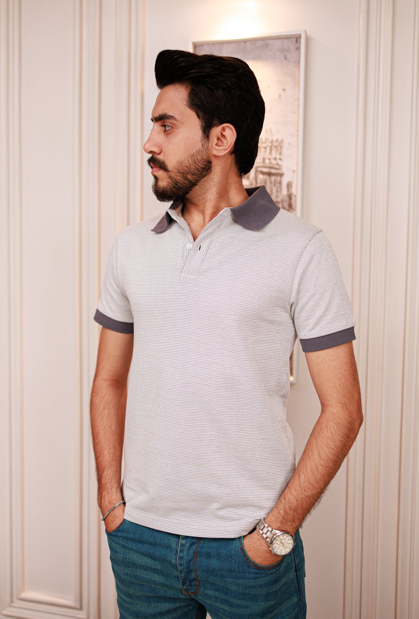 Man wearing a light gray polo shirt with dark trim against a white wall.