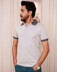 Man wearing a light gray polo shirt with dark trim against a white wall.
