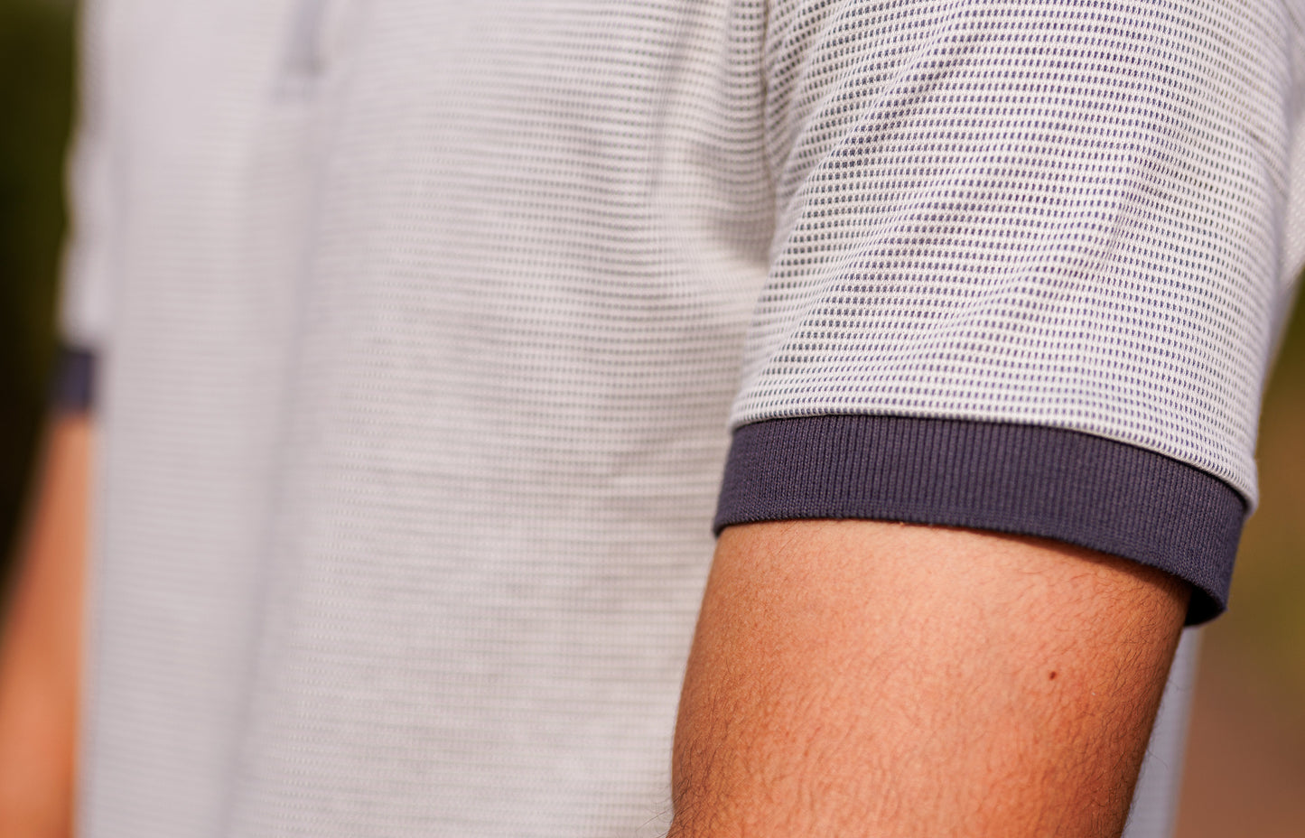 Close-up of a person wearing a light gray shirt with dark blue cuffs.