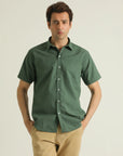 A man wearing a green short-sleeved shirt with a collar, buttoned front, and a straight hem.