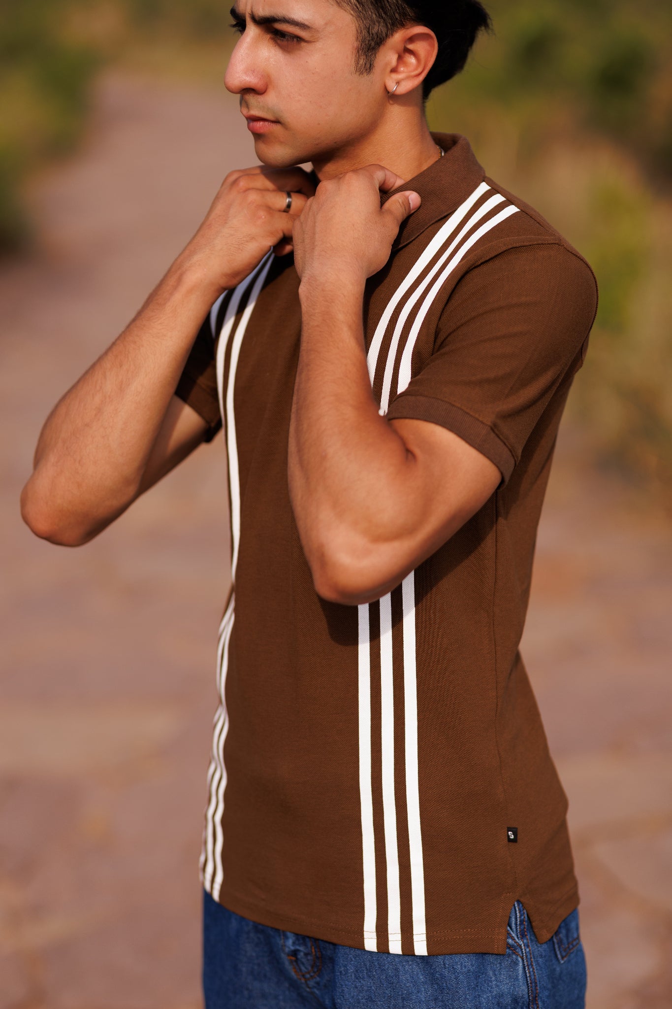 Man wearing a brown shirt with white stripes, standing outdoors.