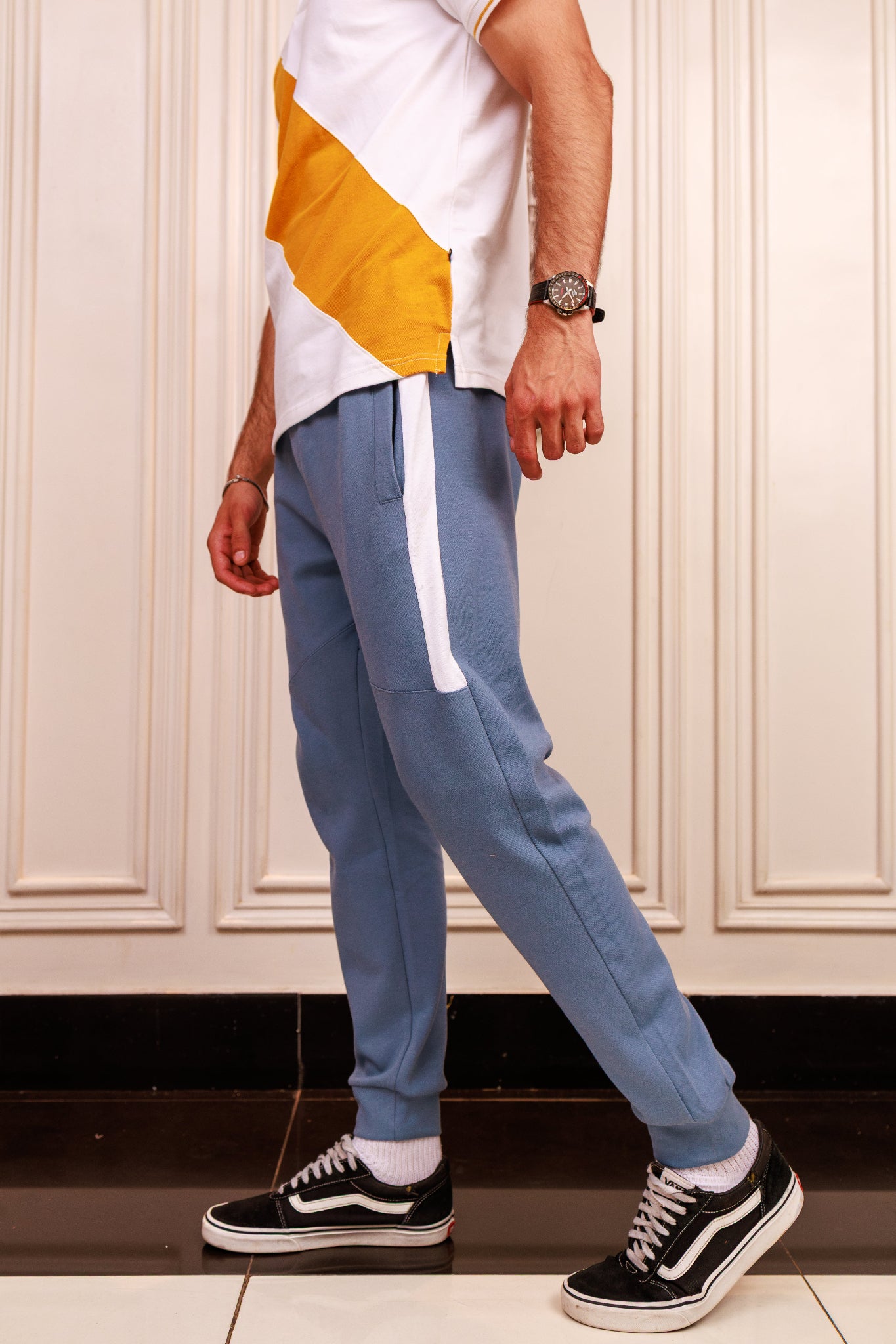 Person wearing blue track pants with a white stripe, white shirt, and black and white sneakers in a room.