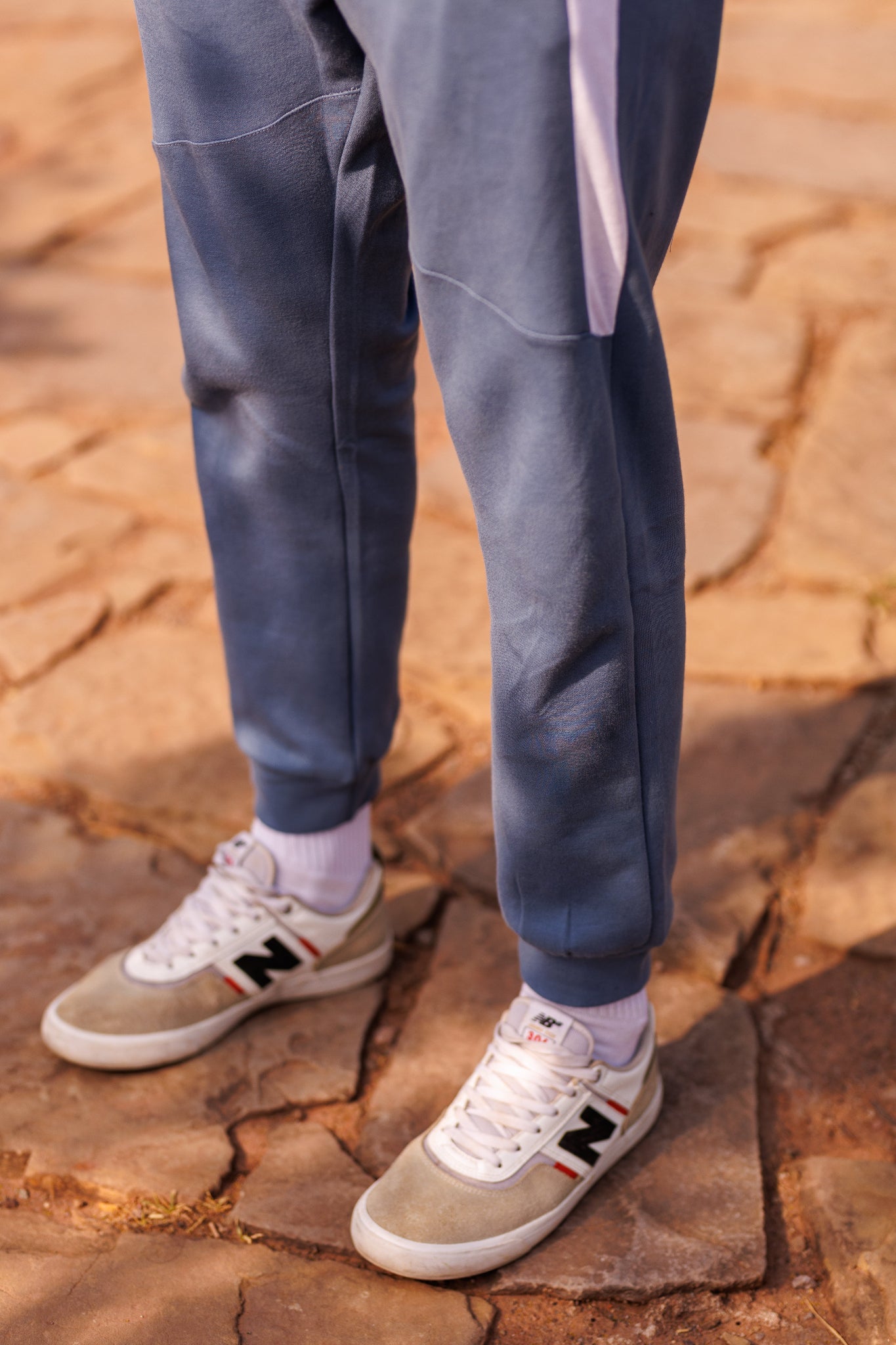 Person wearing blue pants and beige sneakers with black logo on a rocky surface