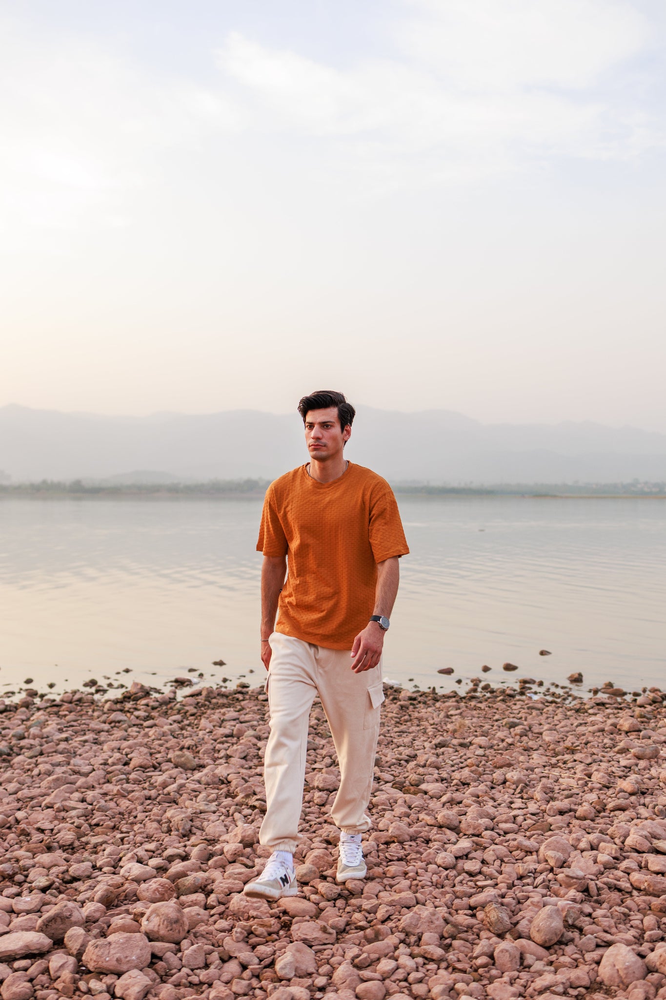 Man standing on a rocky beach with a body of water in the background