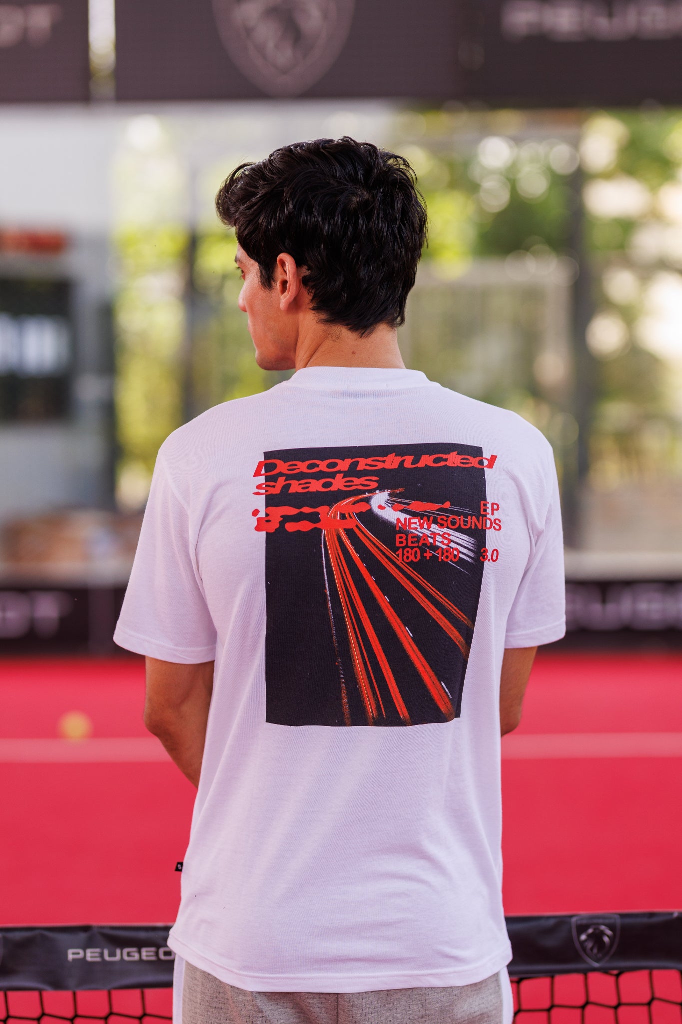 Person wearing a white t-shirt with a black graphic design on the back, standing on a red surface.
