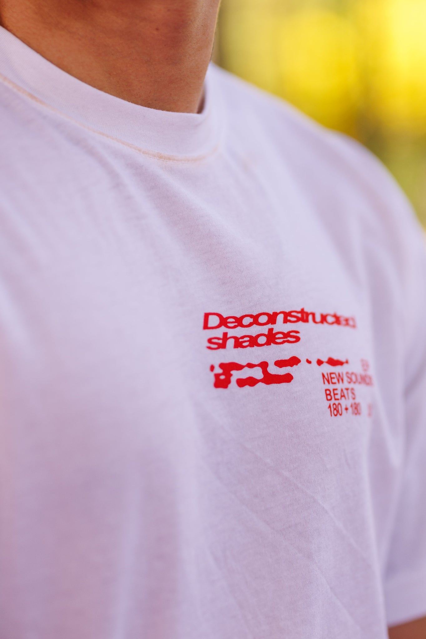 White t-shirt with red text and graphics on a blurred yellow background