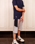 Person wearing a navy t-shirt and gray shorts with a red stripe, standing in a room with white paneled walls.