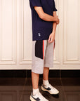 Person wearing a navy t-shirt, gray shorts with red and black stripes, and white sneakers in a room.