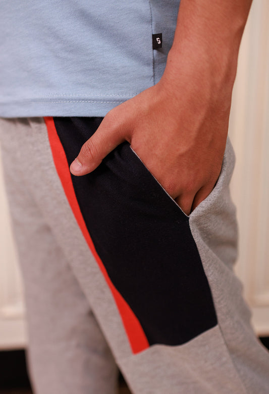 Person wearing gray sweatpants with a black and red stripe, light blue shirt, blurred background