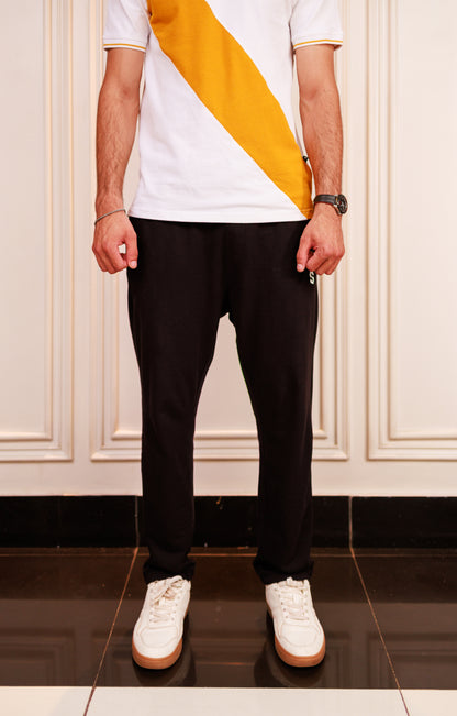 Person wearing a white t-shirt with a yellow stripe, black pants, and white sneakers in a room.