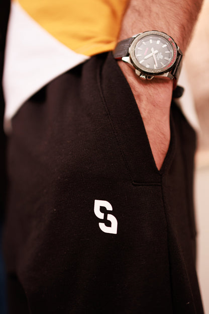 Person wearing a black polo shirt with a white logo and a yellow and white shirt underneath, focusing on the watch.